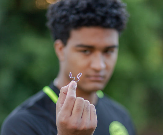 An image of an athlete holding a silent mammoth nasal dilator to the camera. The background is blurred trees with a focus on the nasal dilator.